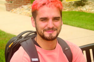 White male with short beard and short pink hair poses for a photo.