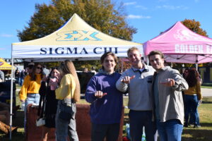 Three male students stand in front of a Sigma Chi tent.