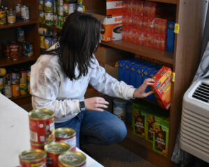Woman with black hair kneels down as she stocks shelves with food.