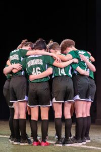 Nine women dressed in soccer uniforms huddle in a circle.