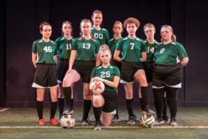 Nine women wearing soccer uniforms pose in a group.